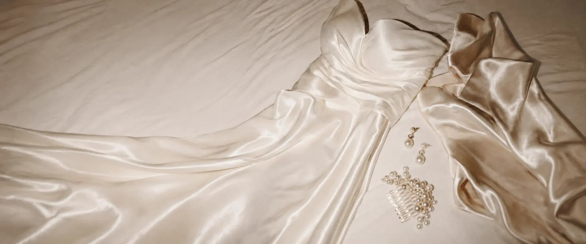 Vestido de novia de satén extendido sobre lino con joyas de perlas